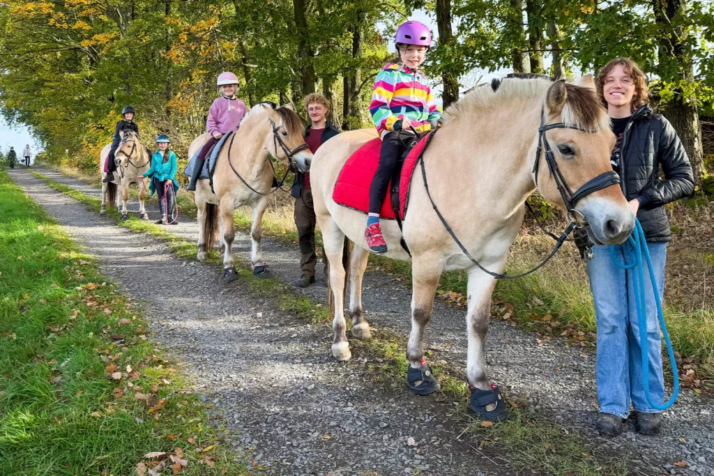 Kinder auf Fjordpferden bei einem begleiteten Ausritt durch den Herbstwald während der Reiterferien am Landgut Kemper & Schlomski 2026.