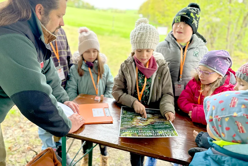 Grundschüler lernen am Plakat, welcher Müll nicht in den Wald gehört.