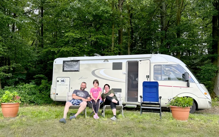 Familie vor ihrem Wohnwagen am Waldrand